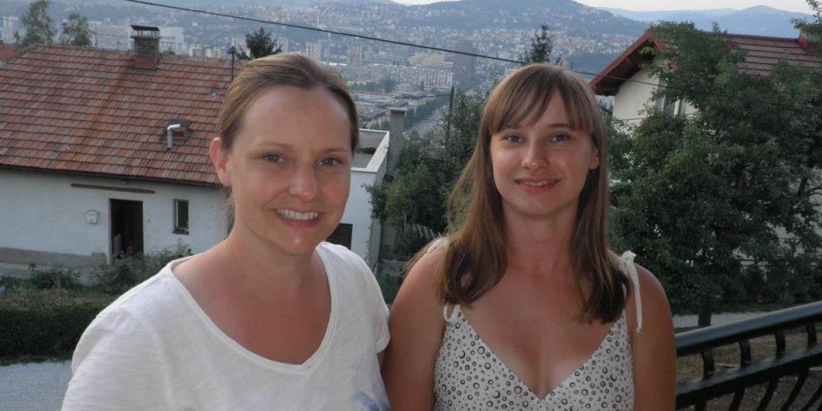 Two women smile on a balcony overlooking a town in Bosnia and Herzegovina