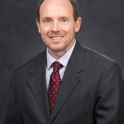 Christian smiles, wearing a gray suit and red tie