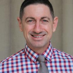 Morgan smiles in a red and white checkered shirt with gray tie